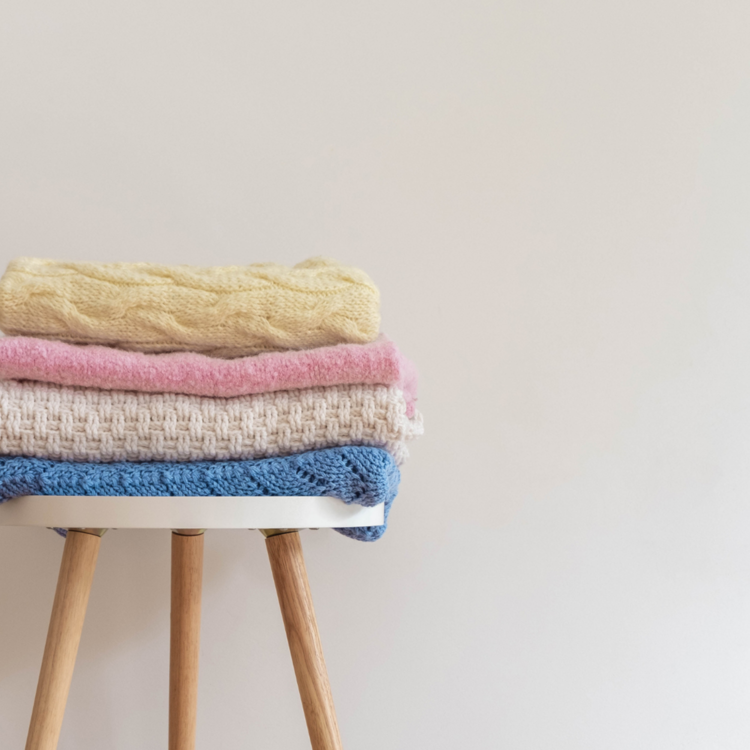 A stack of vibrant knitted blankets neatly arranged on a wooden stool
