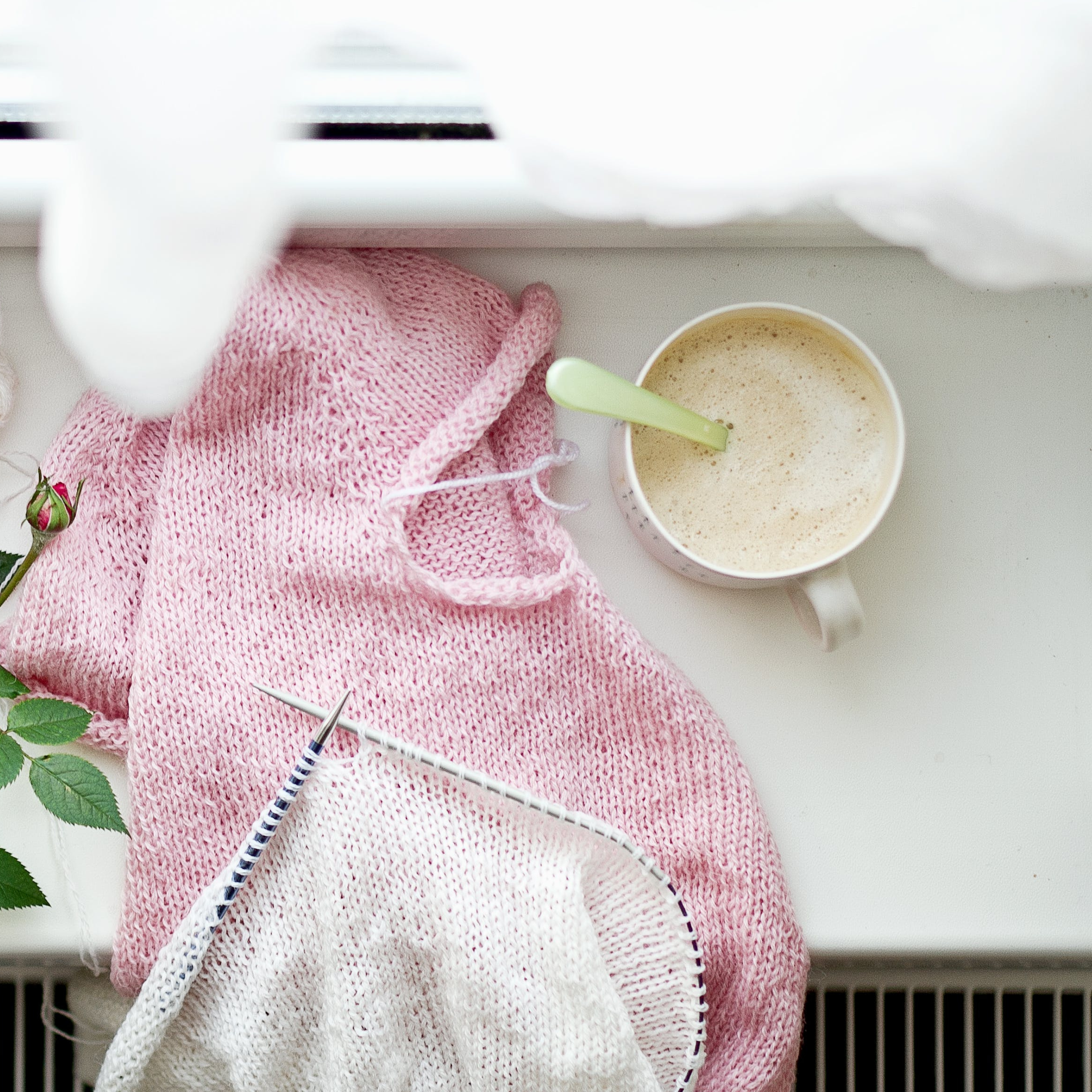 A pink knitting project alongside a cup of coffee