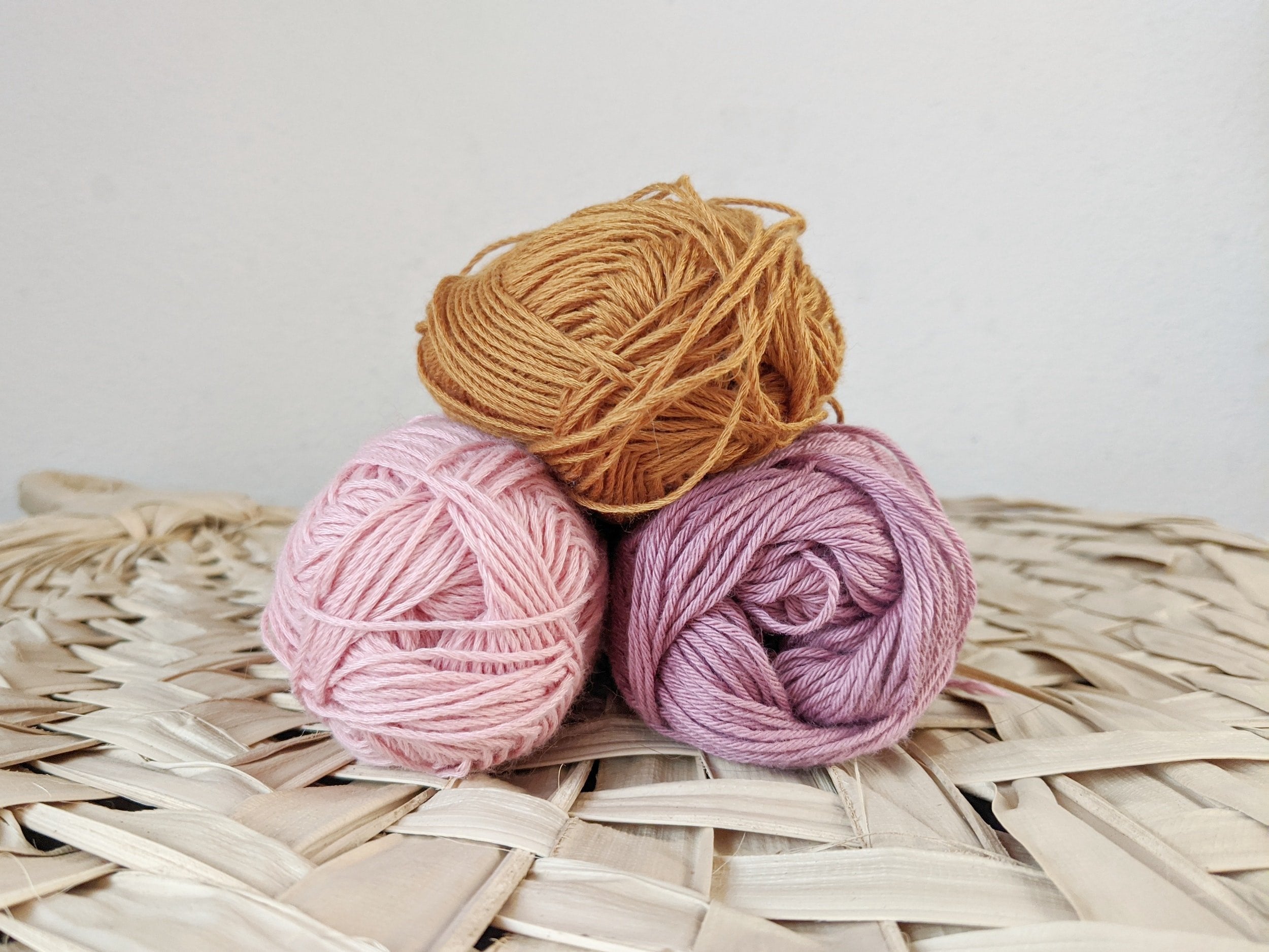 Three colorful balls of yarn neatly arranged on a woven wicker basket