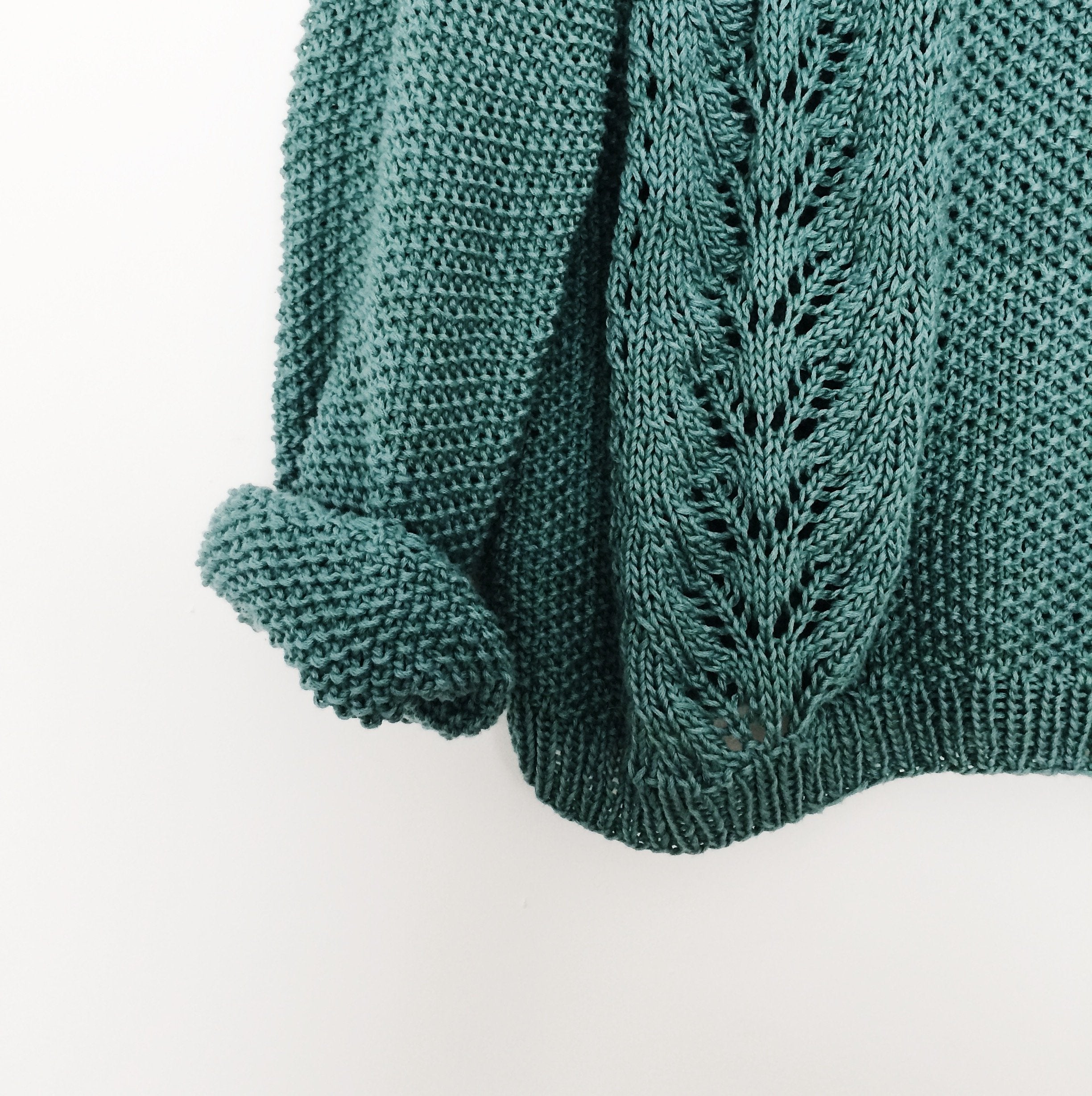 Close-up of a hanging green sweater showcasing an intricate knitted lace design.