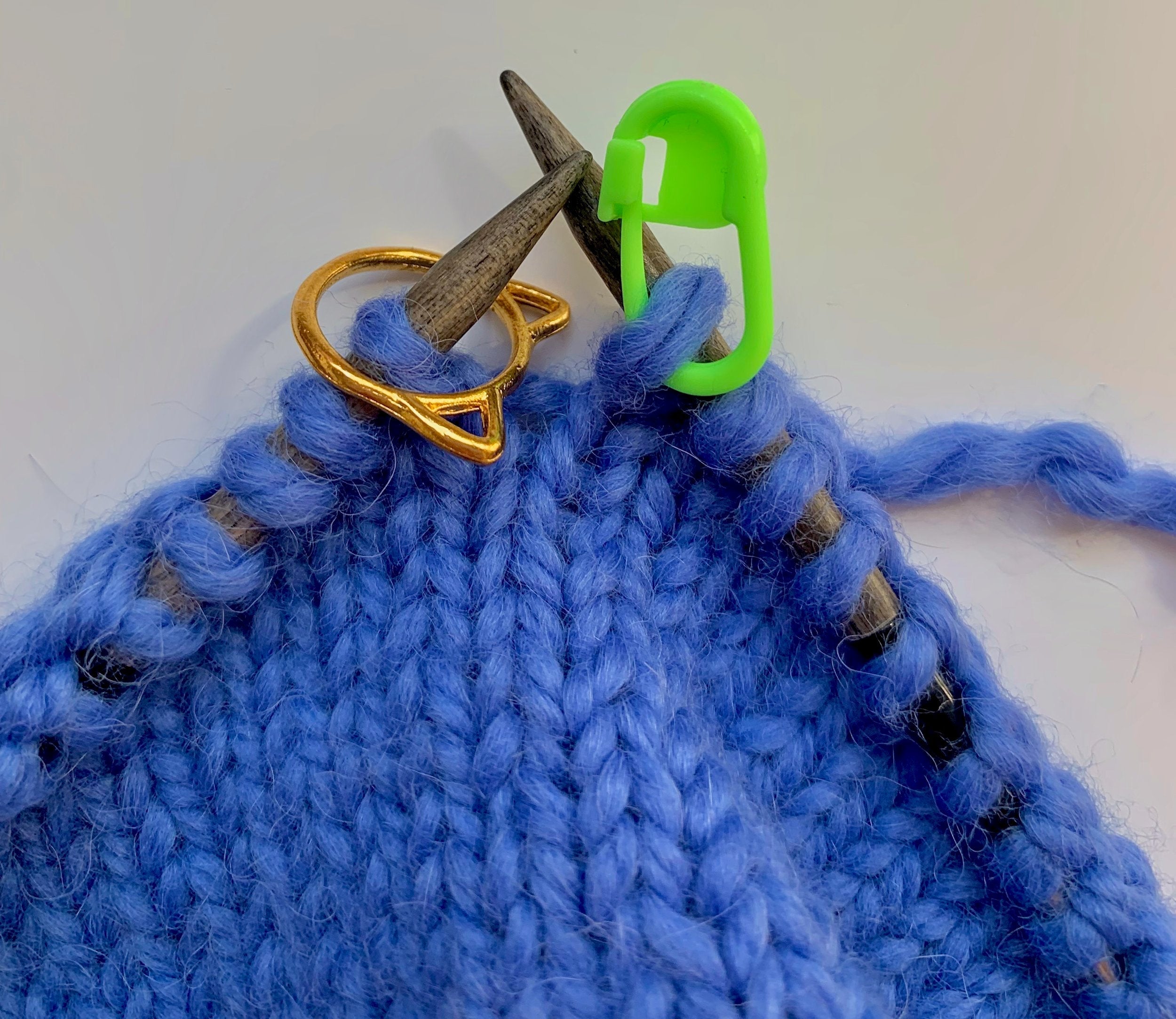 Close-up of knitting project in blue yarn, highlighting removable stitch markers