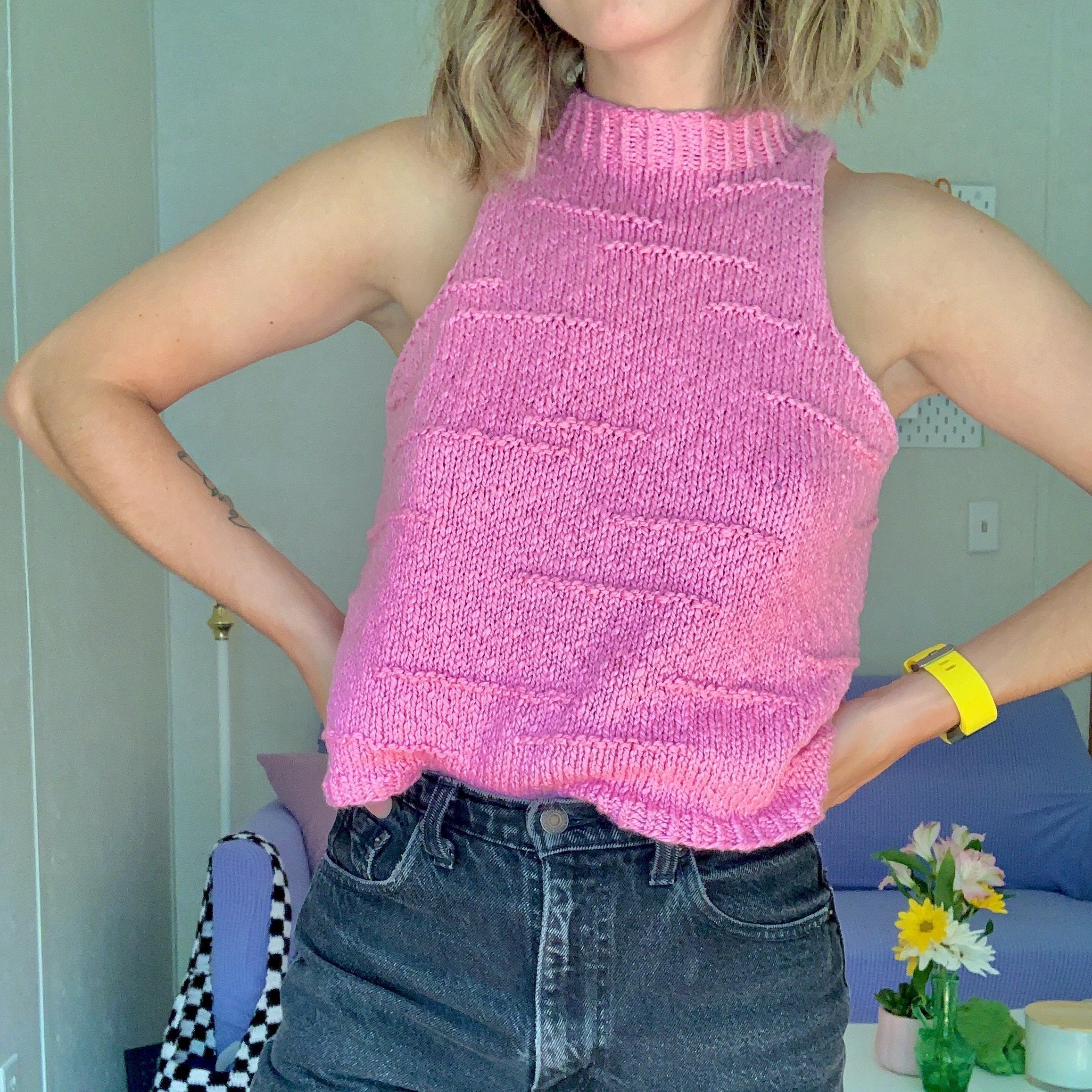 A woman dressed in a pink knitted top and jeans, displaying her trendy knit attire in a casual setting.