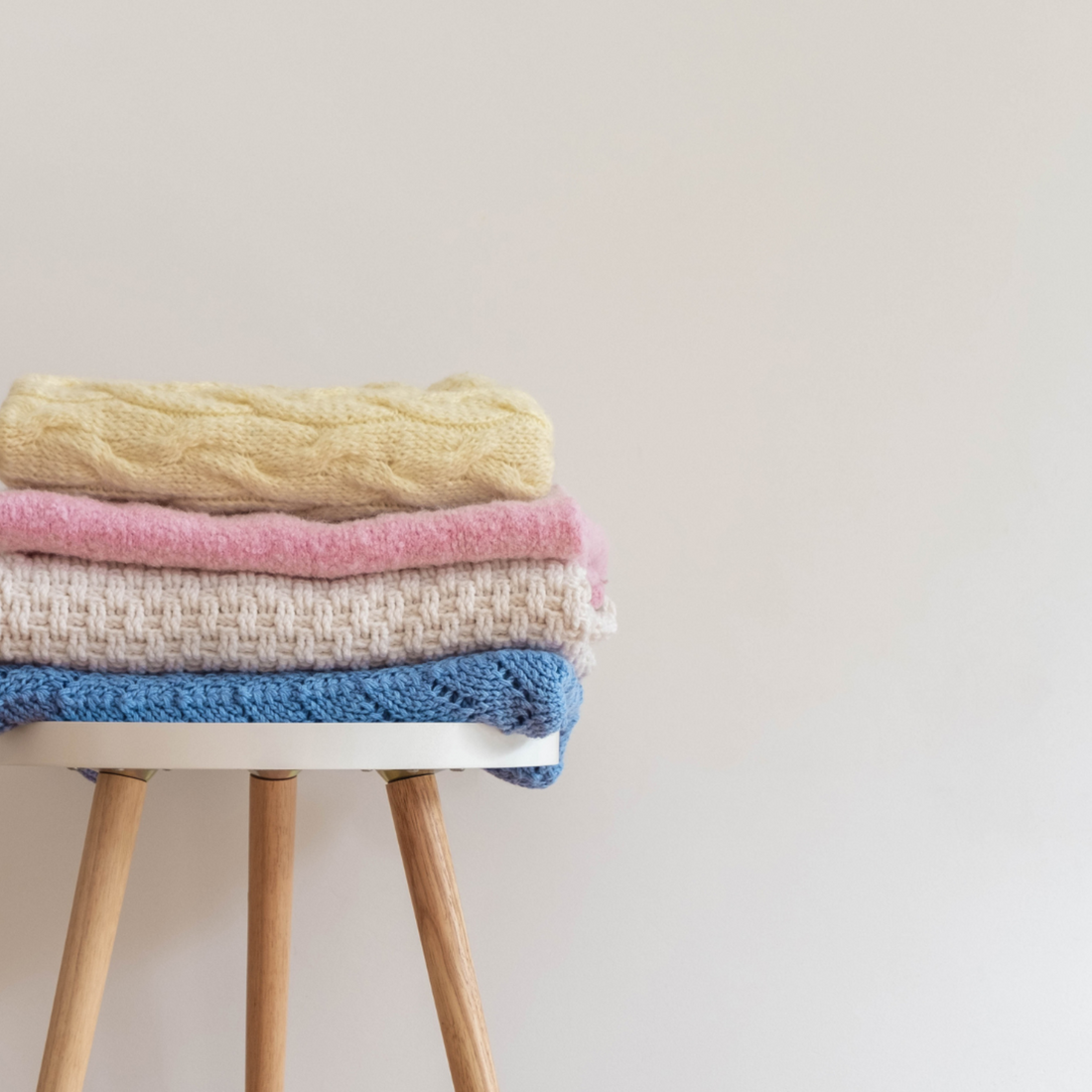 A stack of vibrant knitted blankets neatly arranged on a wooden stool