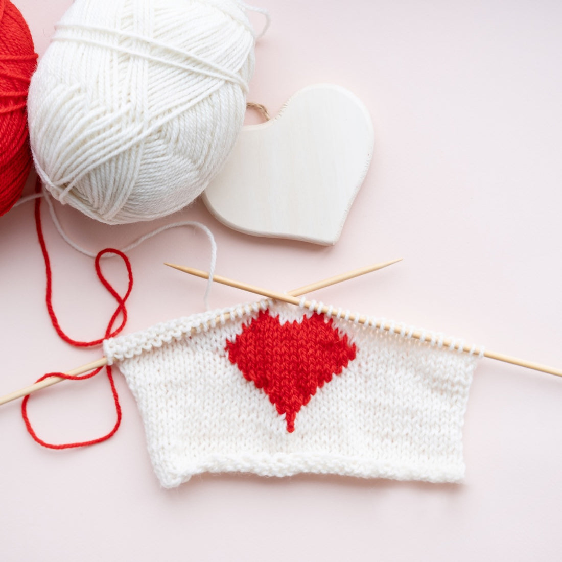 A heart-shaped knitted project with a knitting needle, representing the emotional tales of sweater curses.