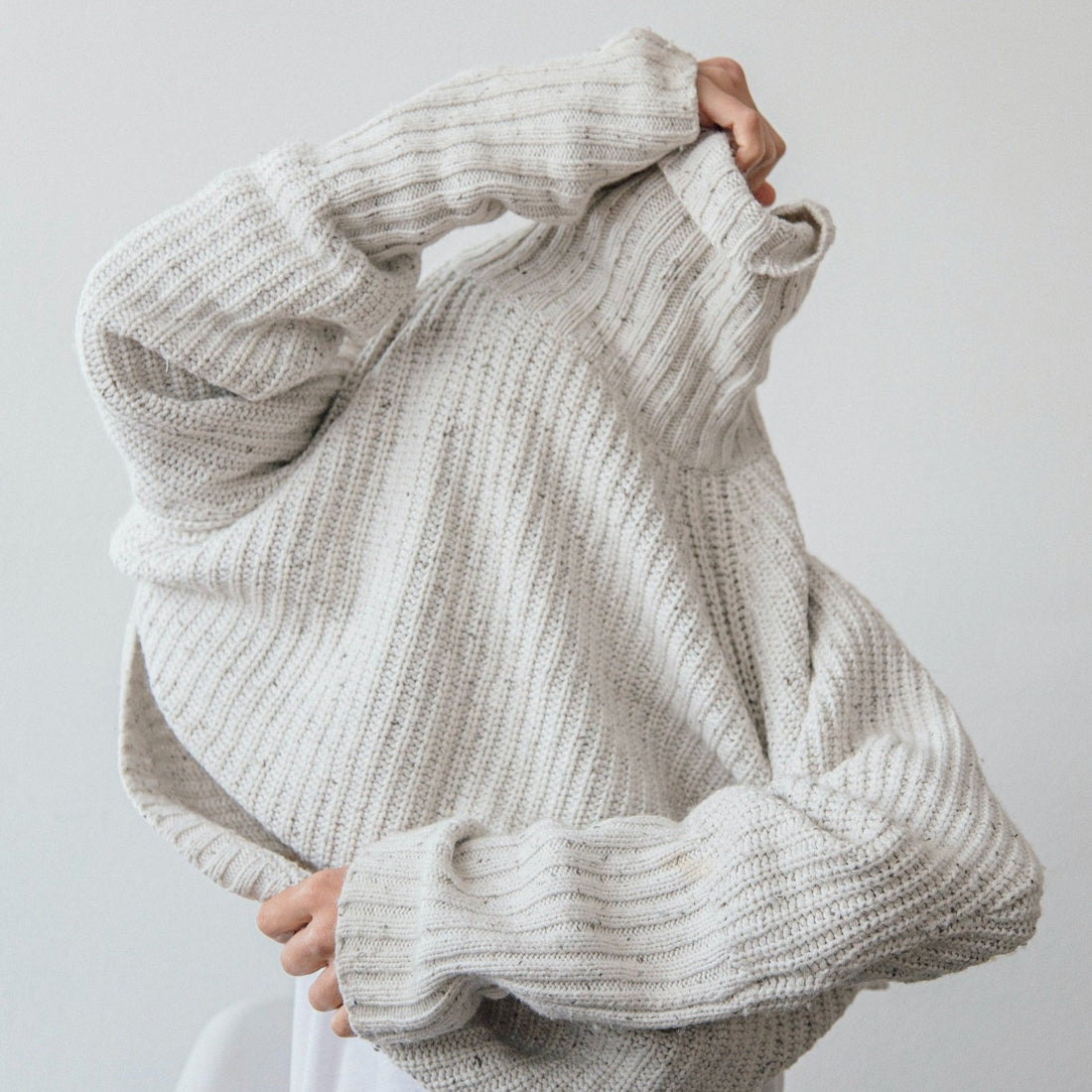 A person pulling a knitted sweater over her face