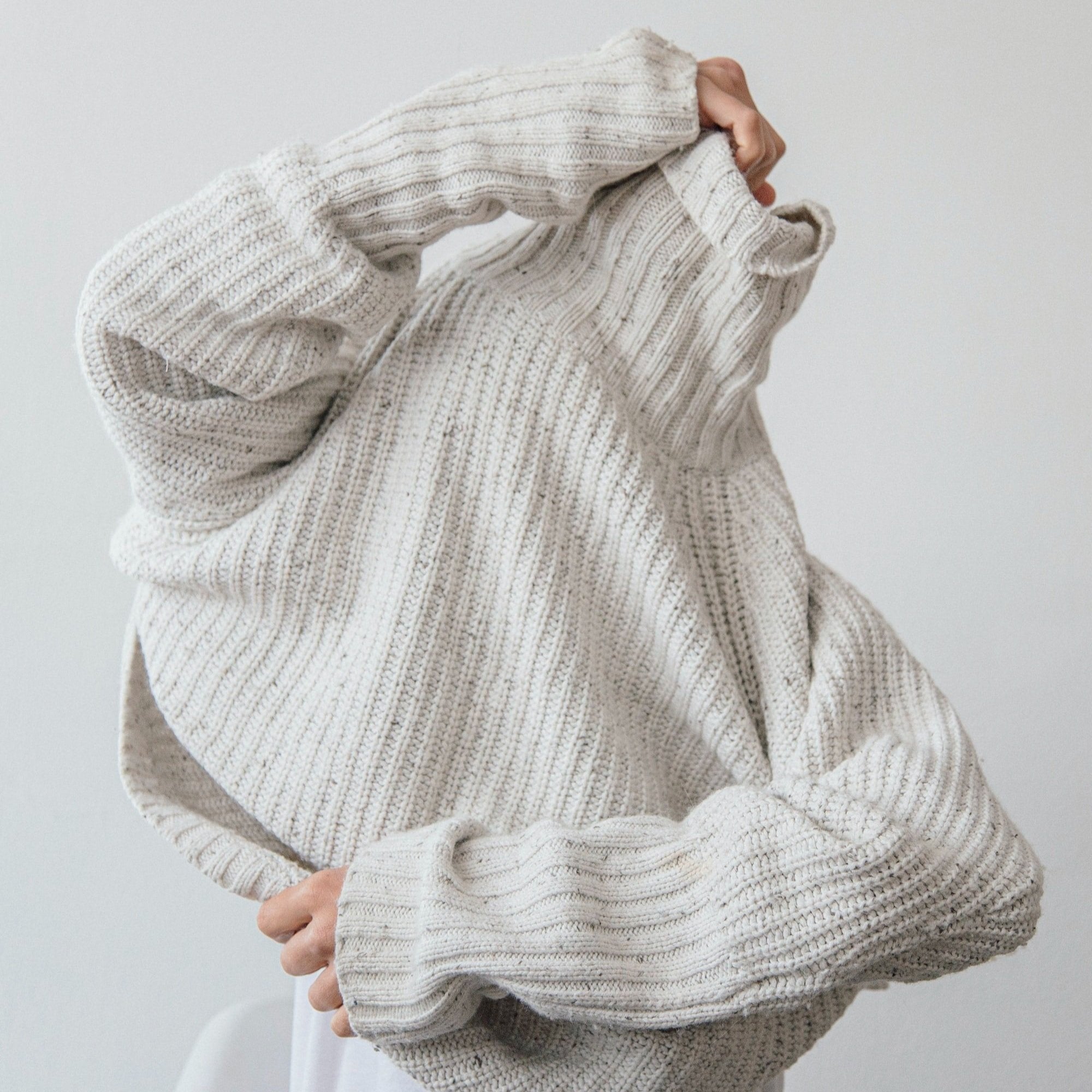 A person pulling a knitted sweater over her face