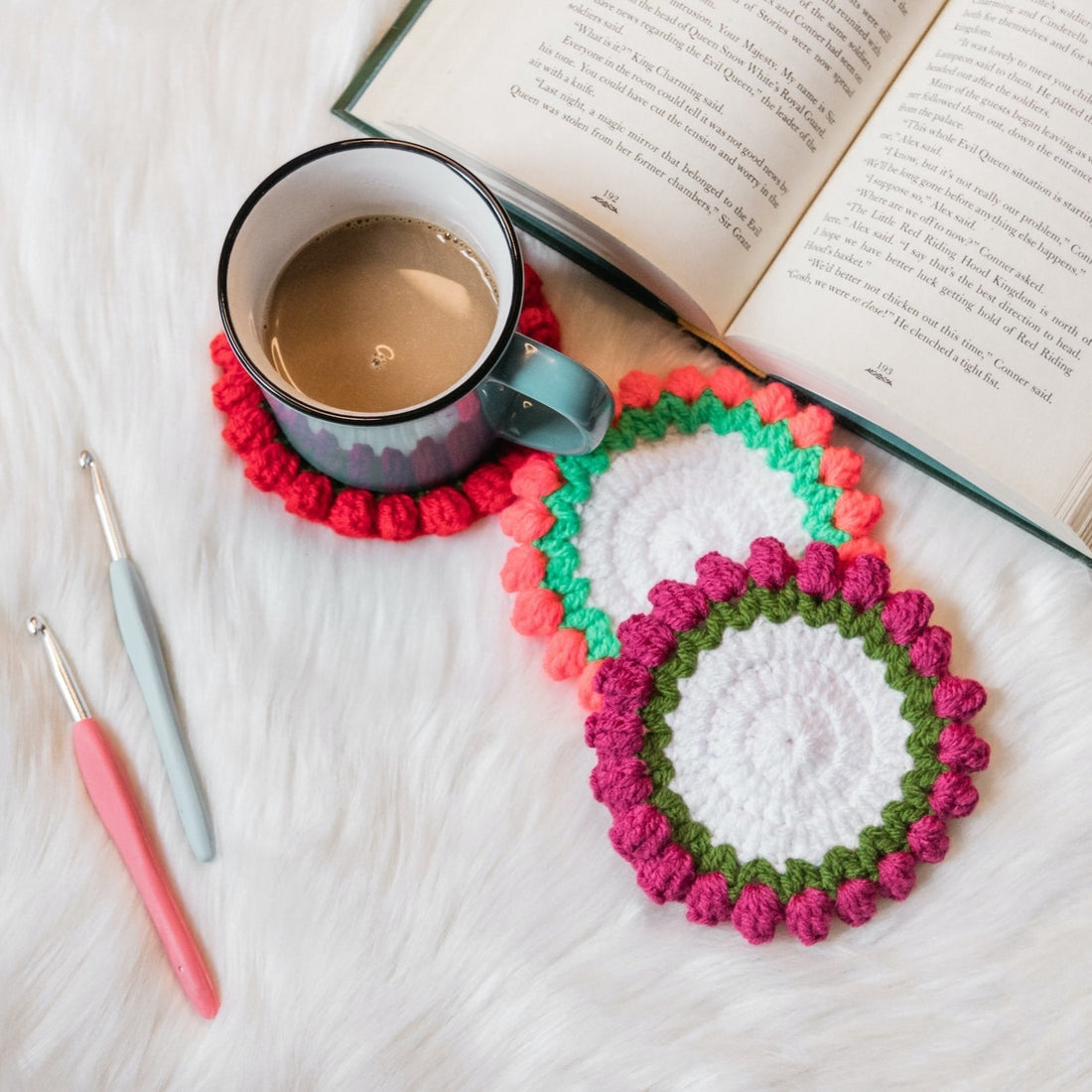 Handmade crochet coasters in vibrant colors beside crochet hooks, and an open book