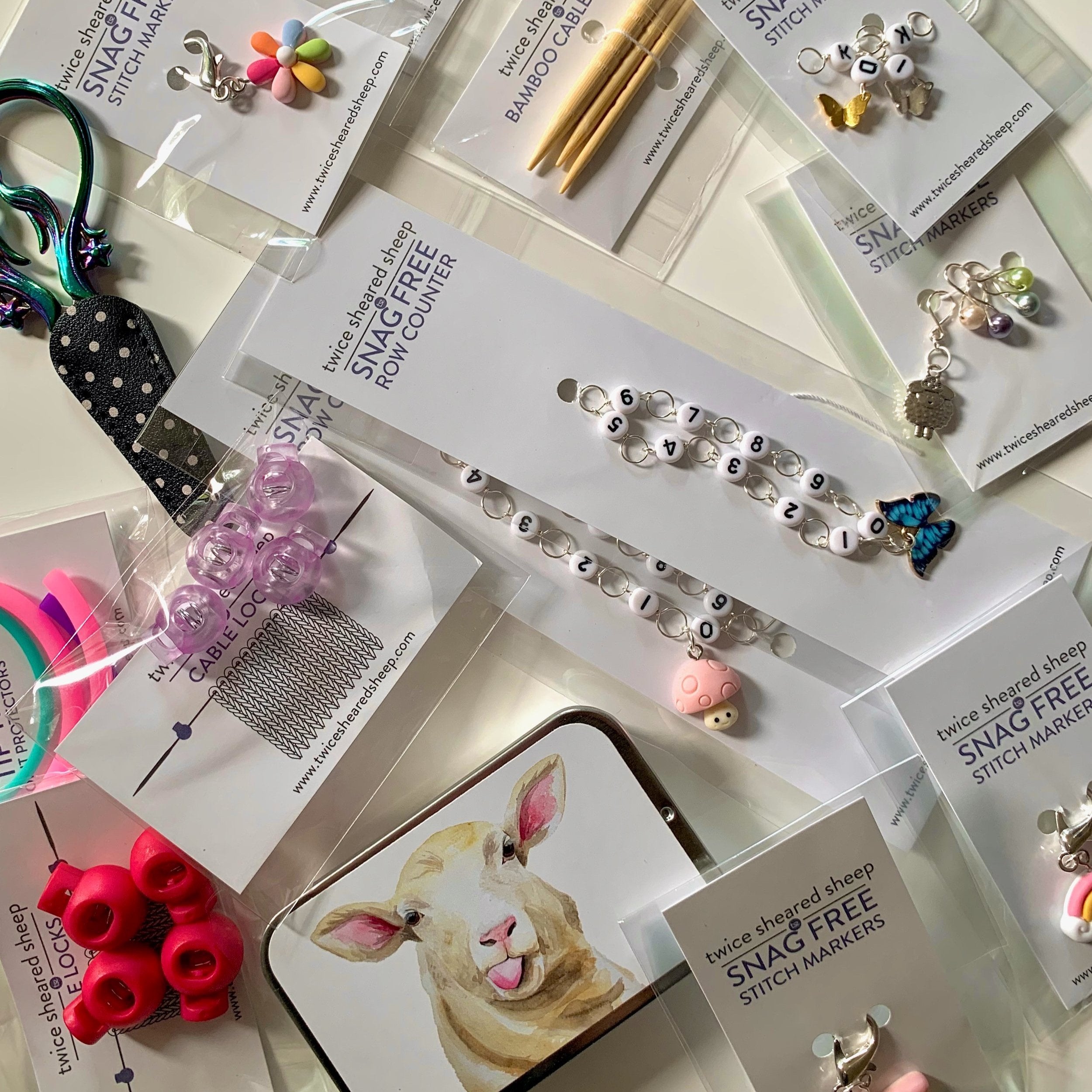 A flat lay of various knitting accessories, including snag-free stitch markers, a row counter bracelet, cable needle protectors, and bamboo cable locks.