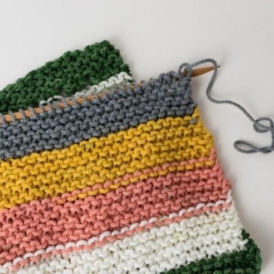 A knitting project featuring horizontal stripes in various colors, including green, gray, yellow, pink, and white, on wooden knitting needles.