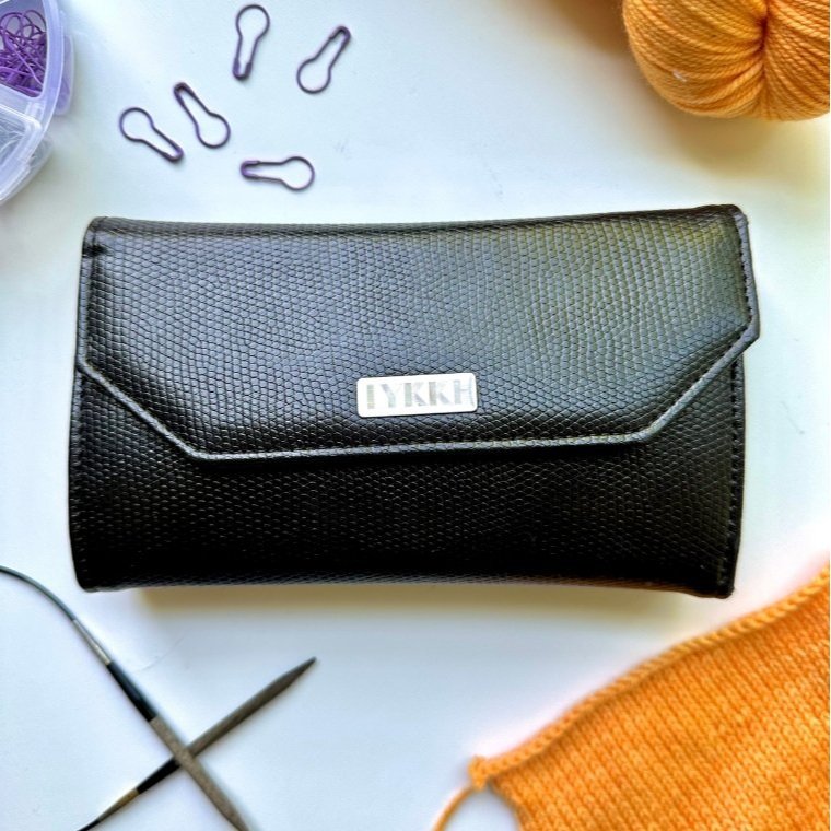 A black knitting needle case with interchangeable needles, stitch markers, and yarn on a white background