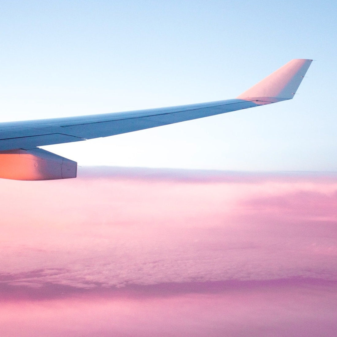 An airplane wing soaring above a stunning pink sky