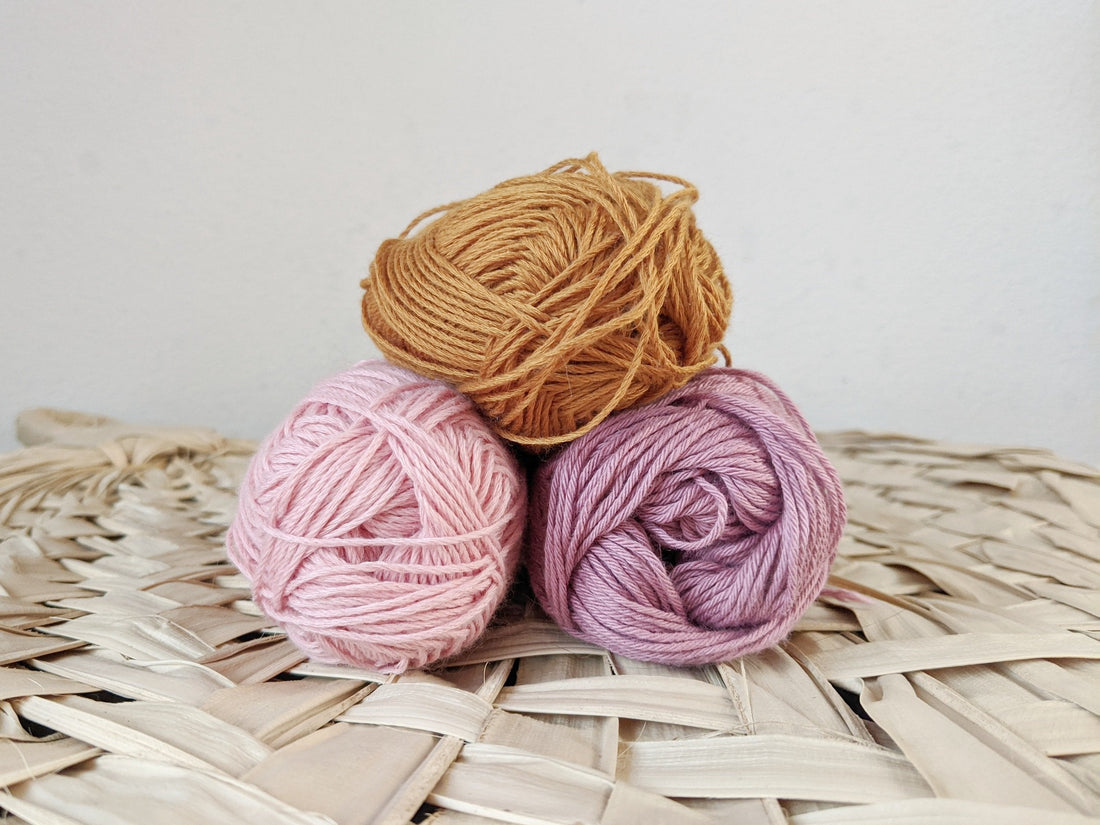 Three colorful balls of yarn neatly arranged on a woven wicker basket