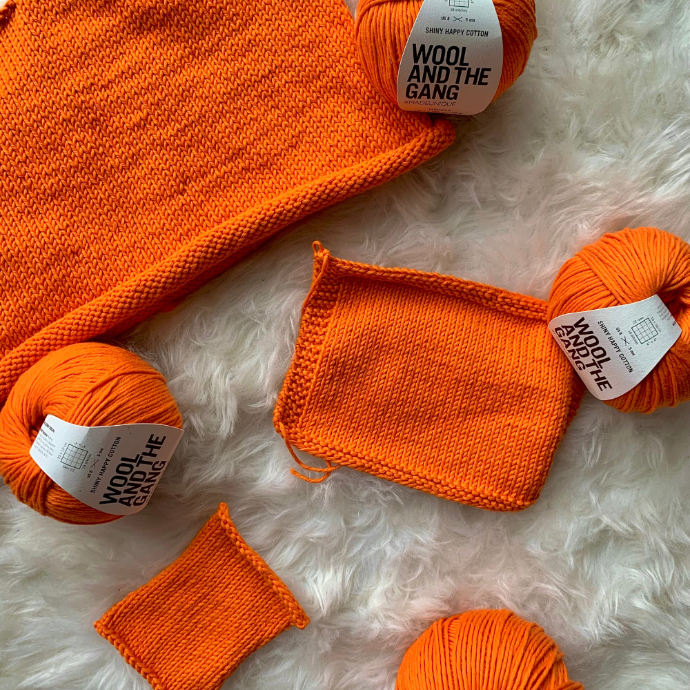 A vibrant orange ball of yarns along with orange knitted projects made from soft cotton yarn from Wool and the Gang