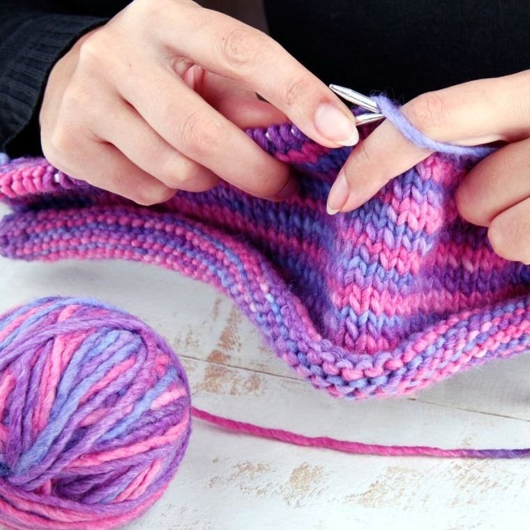 A serene scene of a person knitting with vibrant yarn, creating a beautiful piece of fabric, surrounded by soft lighting.