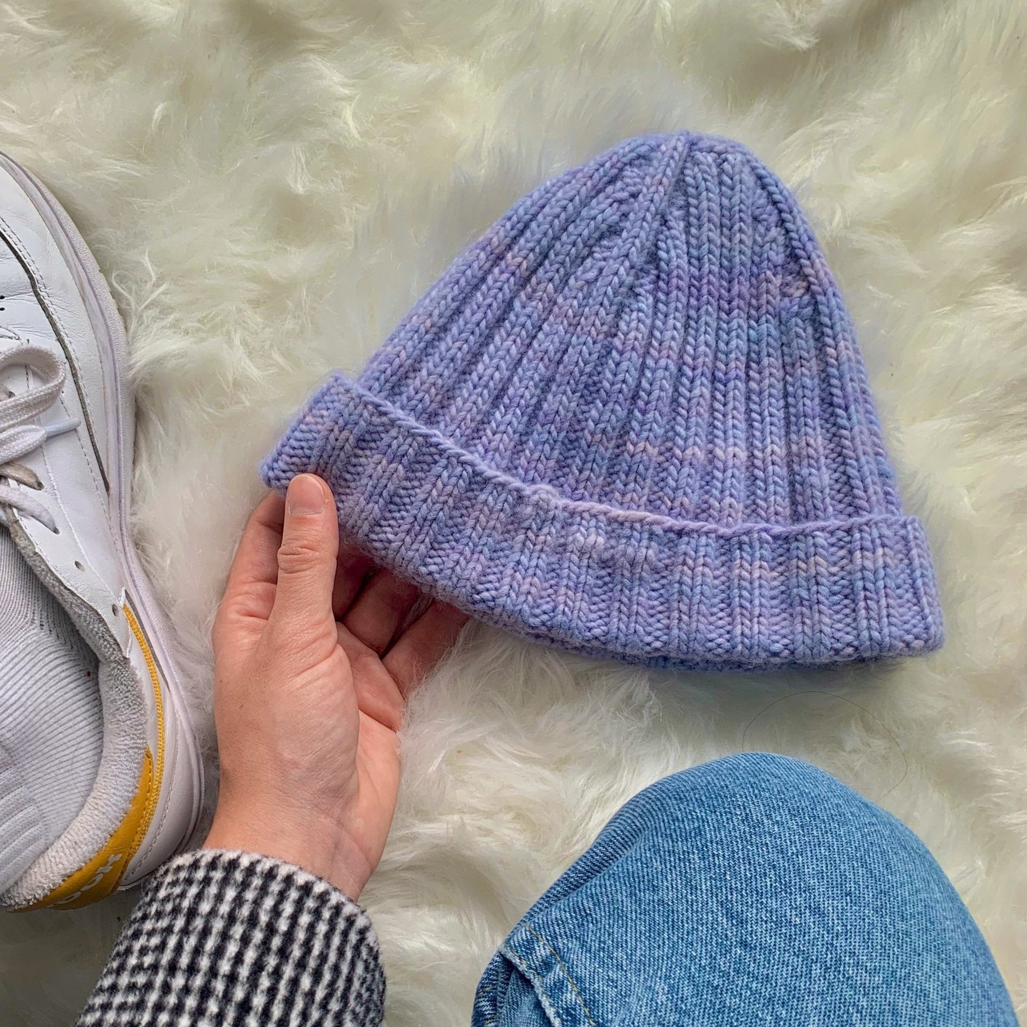 A person in a knit purple hat and white sneakers stands confidently, showcasing a stylish and casual look.