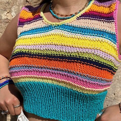A woman in a colorful knit top proudly displays her work as a beginner knitting pattern designer.