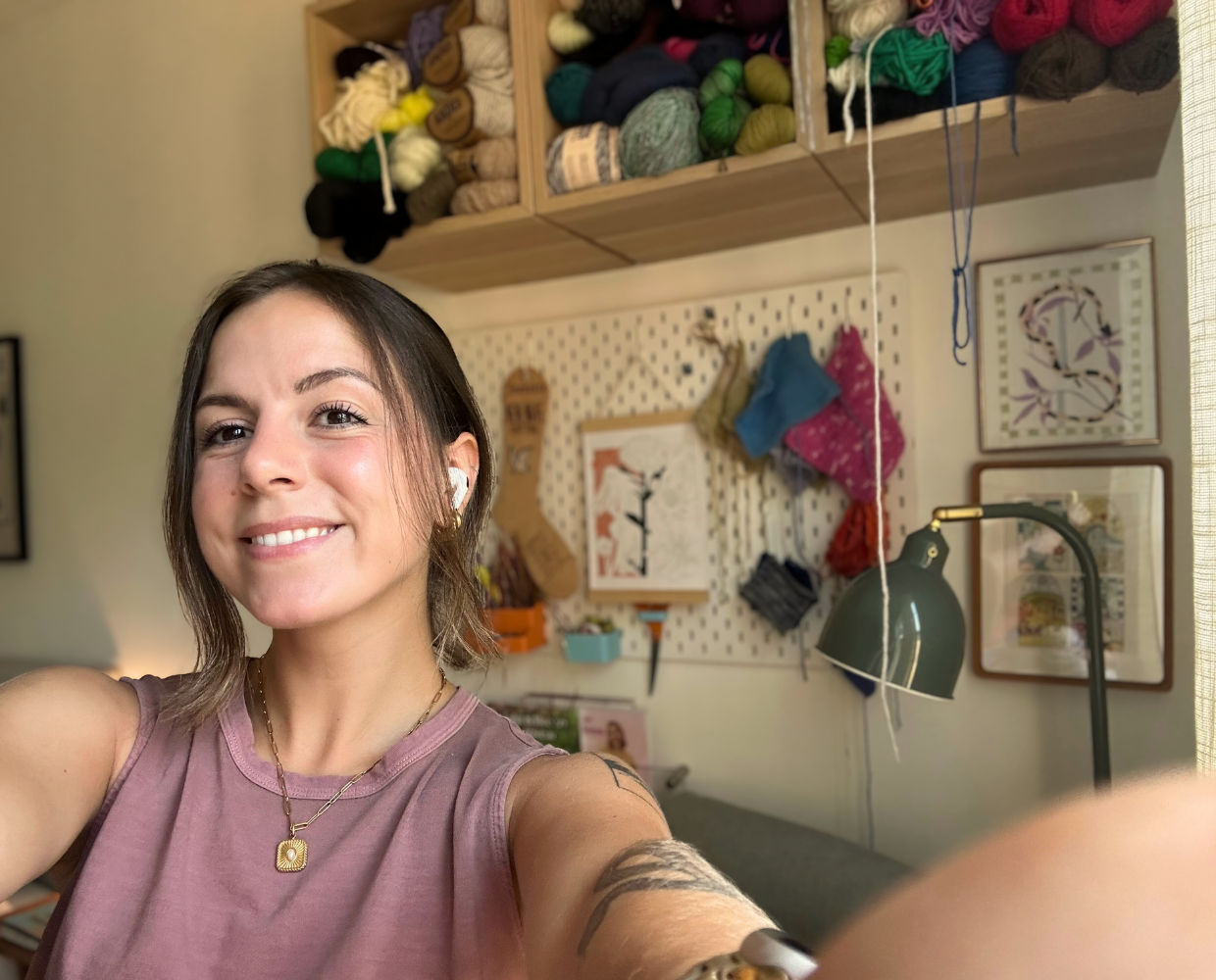 Woman taking a selfie in a craft room with yarn and supplies on shelves.