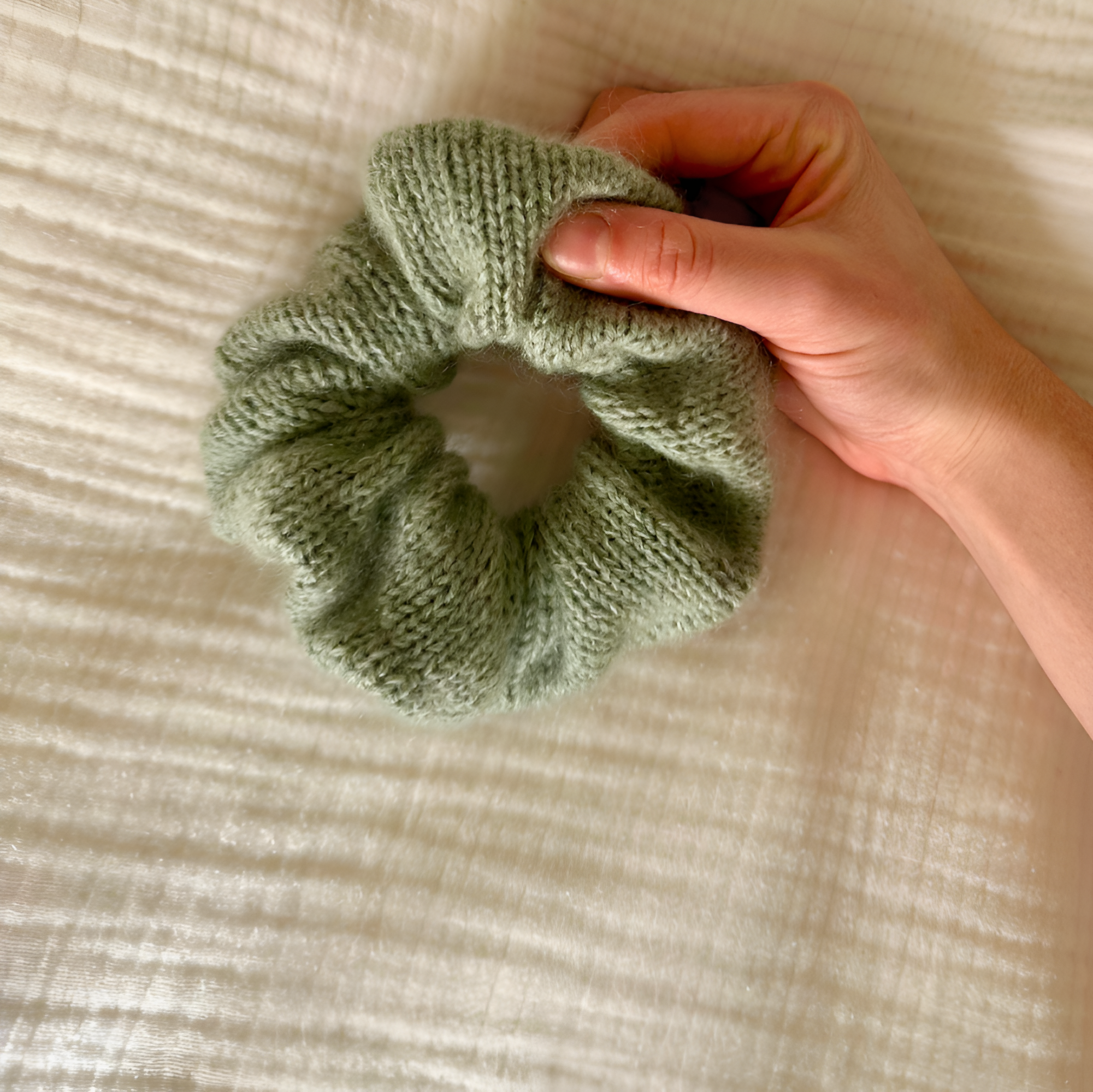 Hand holding a green knitted scrunchie on a beige fabric background