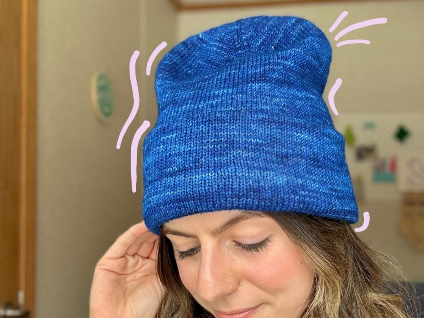 girl showcases a blue knitted hat using the tall staple beanie pattern
