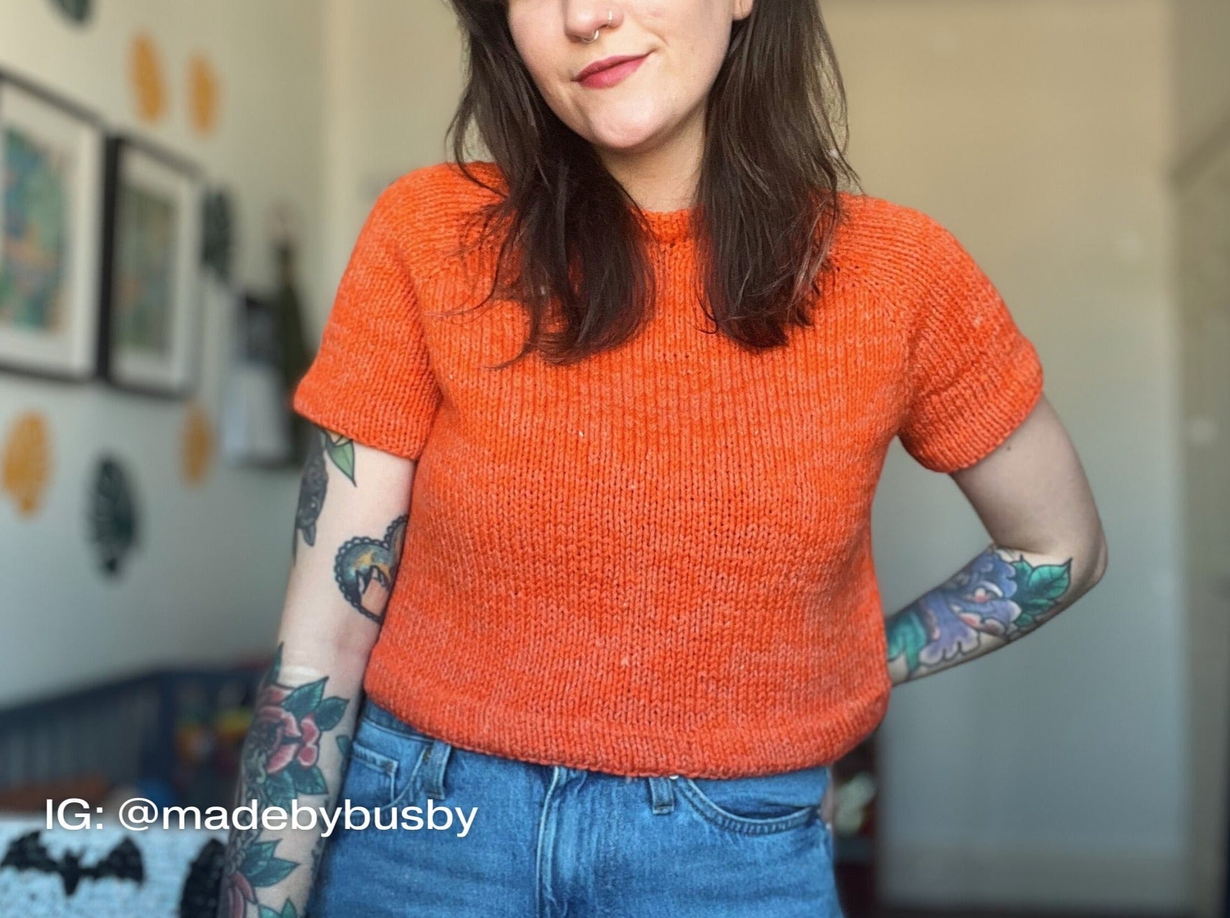 a woman with tattoos in an orange knitted top highlighting The Staple Tee's unique design.
